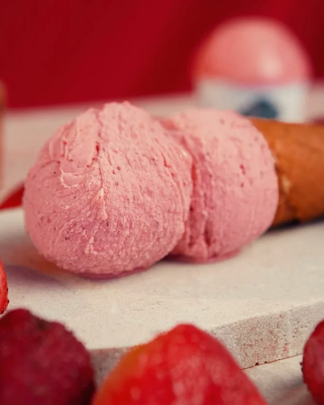 Duas bolas de gelato de morango ao lado de morangos frescos